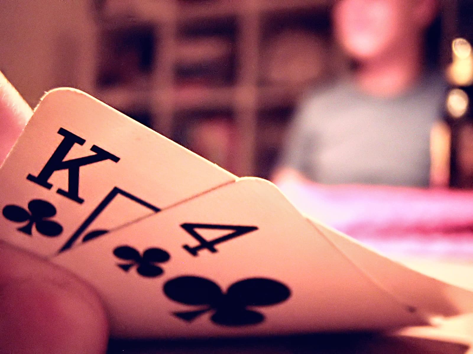 Two hole cards, the king and four of clubs, lifted at the edge of a poker table